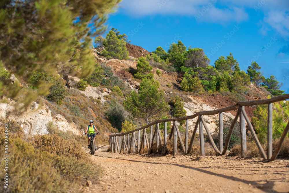 nice active woman riding her electric mountain bike in a cactus desert of the abandoned Iron Ore mines of Calamite peninsula on the Island of Elba, Tuscan Archipelago, Tuscany,Italy 
