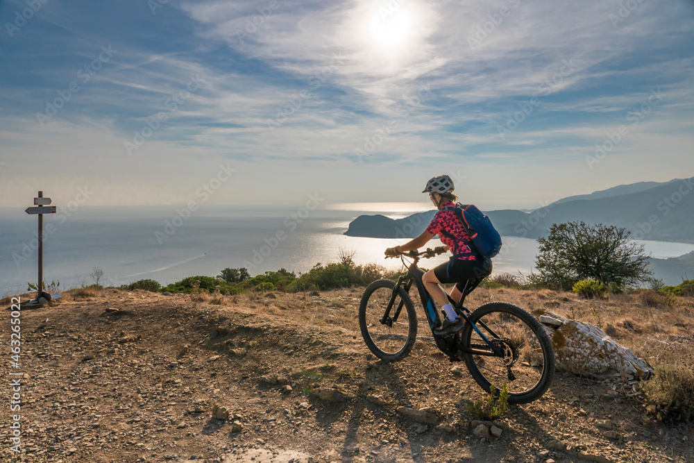 Obraz premium nice woman riding her electric mountain bike at sunset at the coastline of mediterranean sea on the Island of Elba in the tuscan Archipelago Tuscany, Italy