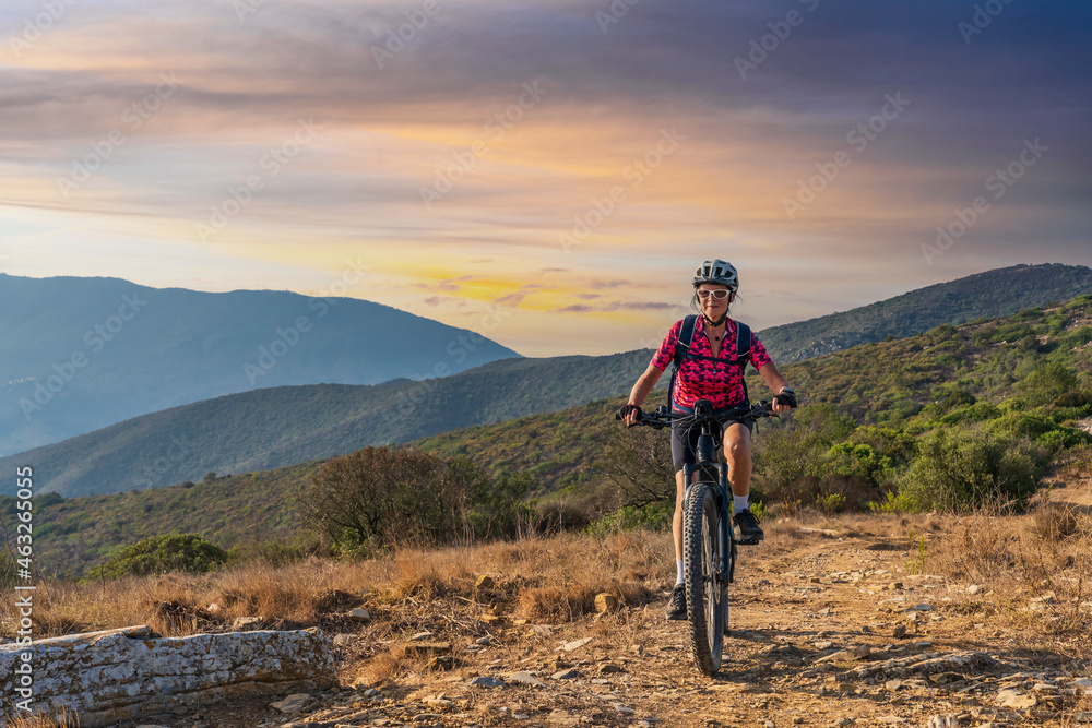 nice woman riding her electric mountain bike at sunset at the coastline of mediterranean sea on the Island of Elba in the tuscan Archipelago Tuscany, Italy