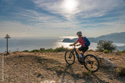 Fototapeta Naklejka Na Ścianę i Meble -  nice woman riding her electric mountain bike at sunset at the coastline of mediterranean sea on the Island of Elba in the tuscan Archipelago Tuscany, Italy