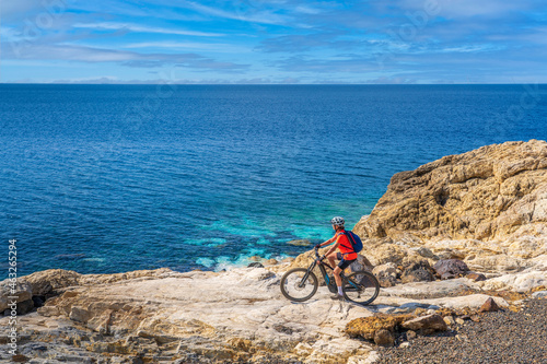 nice woman riding her electric mountain bike at the coastline of mediterranean sea on the Island of Elba in the tuscan Archipelago, in front of Porto Ferraio,Tuscany, Italy