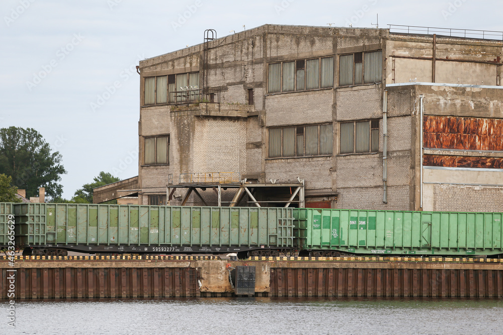 Fototapeta premium Old brick building with train tracks and cargo train standing nearby. Cargot rain in green color.
