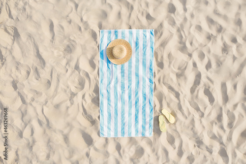 Fototapeta Naklejka Na Ścianę i Meble -  Striped beach towel, straw hat and flip flops on sand, aerial view