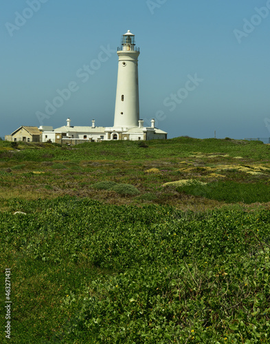 An old whitewashed lighthouse seen over a stretch of dune vegetation with the Indian Ocean behind it