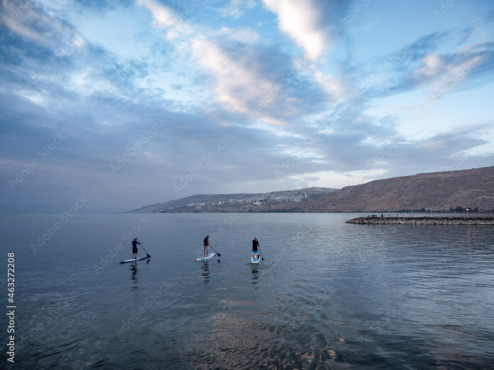 Three men float on a surfboard and row the Kinneret in the early morning at dawn.