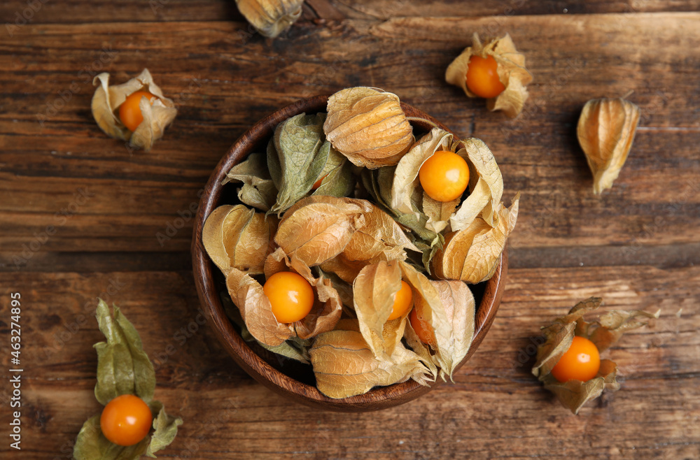 Fototapeta premium Ripe physalis fruits with dry husk on wooden table, flat lay