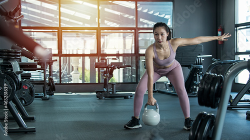 person exercising in gym.  Woman in exercise gear standing and holding dumbbells during an exercise class at the gym. Fitness training with kettlebell in sport gym.