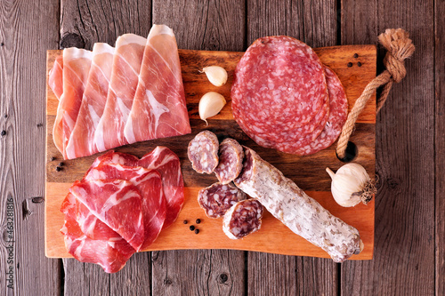 Meat appetizer platter with sausage, prosciutto, ham and salami. Overhead view on a serving board against a wood background. photo