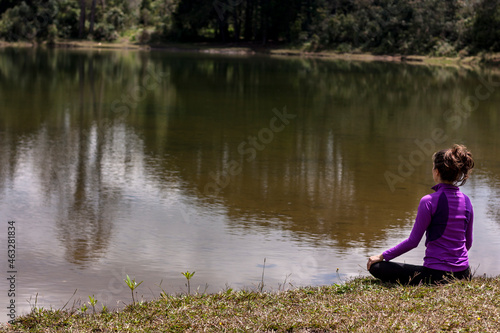 Woman sitting on her back meditating in front of a pond with Cloud reflections in the water.