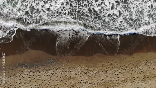 Drone view of beautiful endless images in ultra slow motion as the foamy waves break on the sandy shore. Aerial shot of a golden beach meeting deep ocean waters.