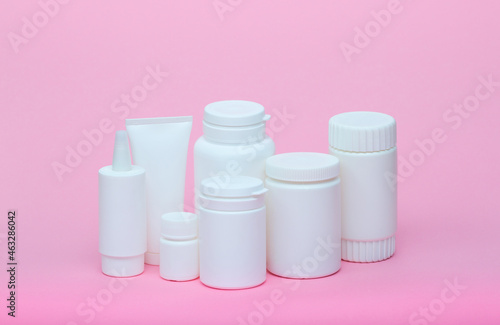 White different medecine or cosmetic jars on a pink background as a concept of cosmetology of medecine and treatment