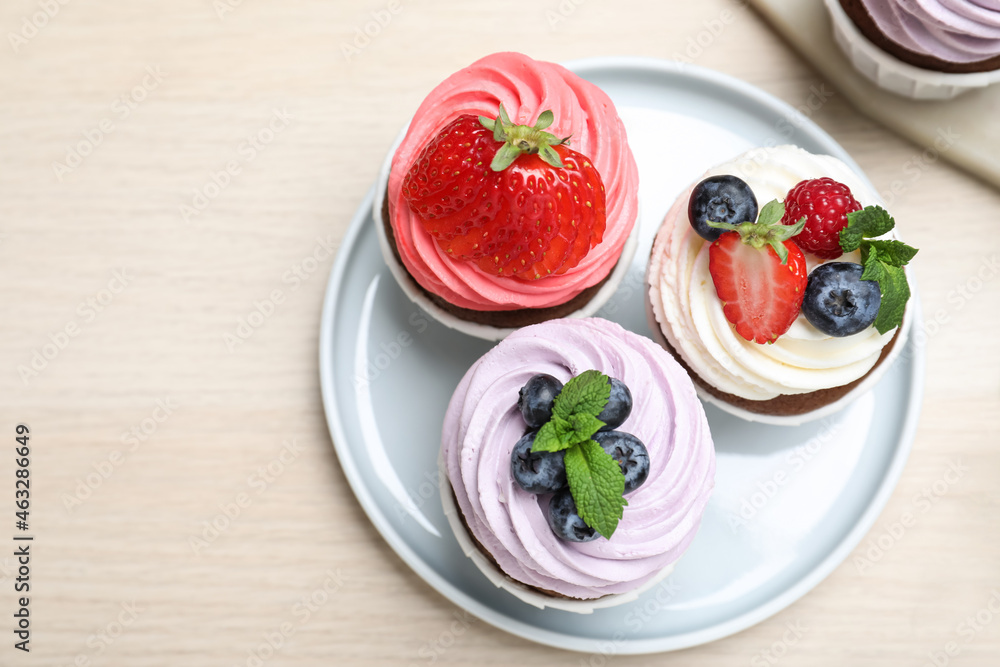 Sweet cupcakes with fresh berries on light wooden table, flat lay. Space for text Sweet cupcakes with fresh berries on light wooden table, flat lay. Space for text
