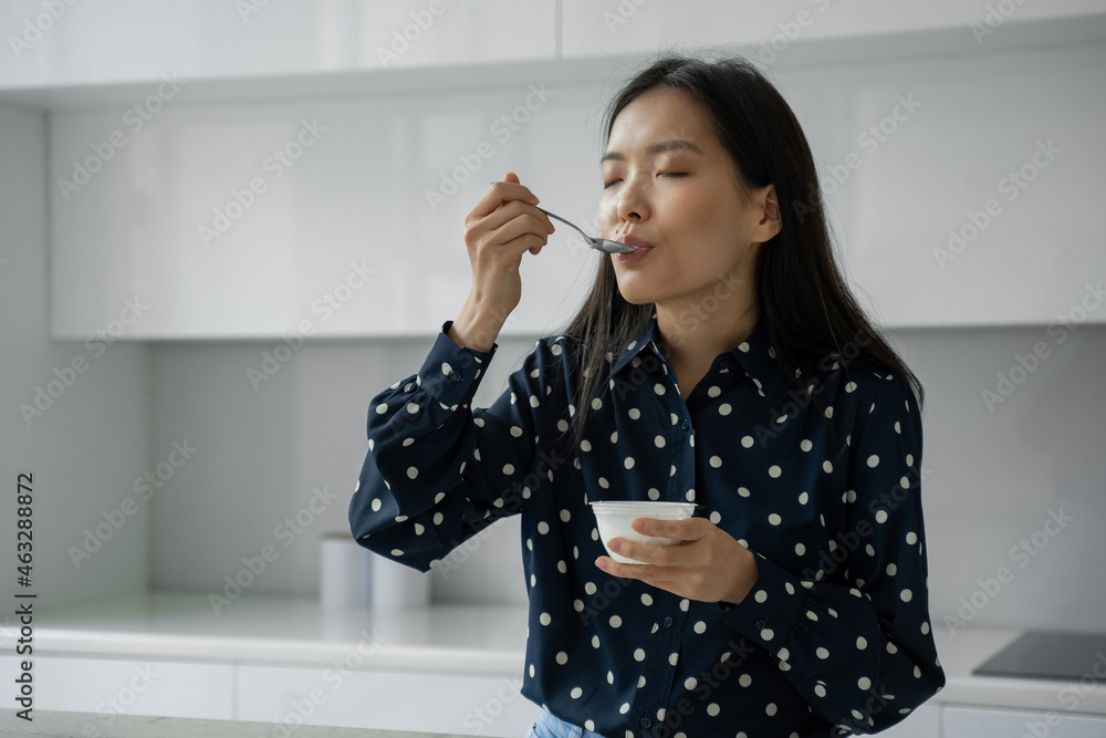 Young Asian woman eats fresh yogurt for breakfast in the kitchen Young Asian woman eats fresh yogurt for breakfast in the kitchen