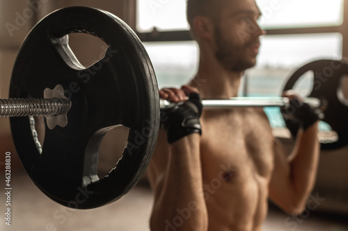 Crop strong bodybuilder raising barbell in gym