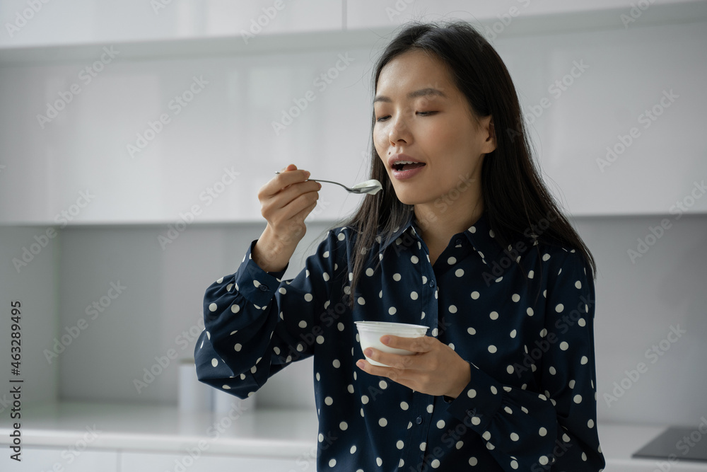 Young Asian woman eats fresh yogurt for breakfast in the kitchen Young Asian woman eats fresh yogurt for breakfast in the kitchen