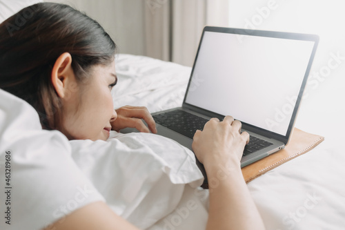 Asian woman works with laptop on the bed in concept of workation.