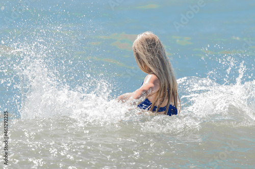 Young cheerful girl teenager blonde makes splashes of water with her hands in the sea