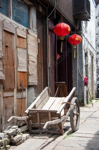 An ancient alley with an old wooden cart parked on the left side with some red lampions lining up