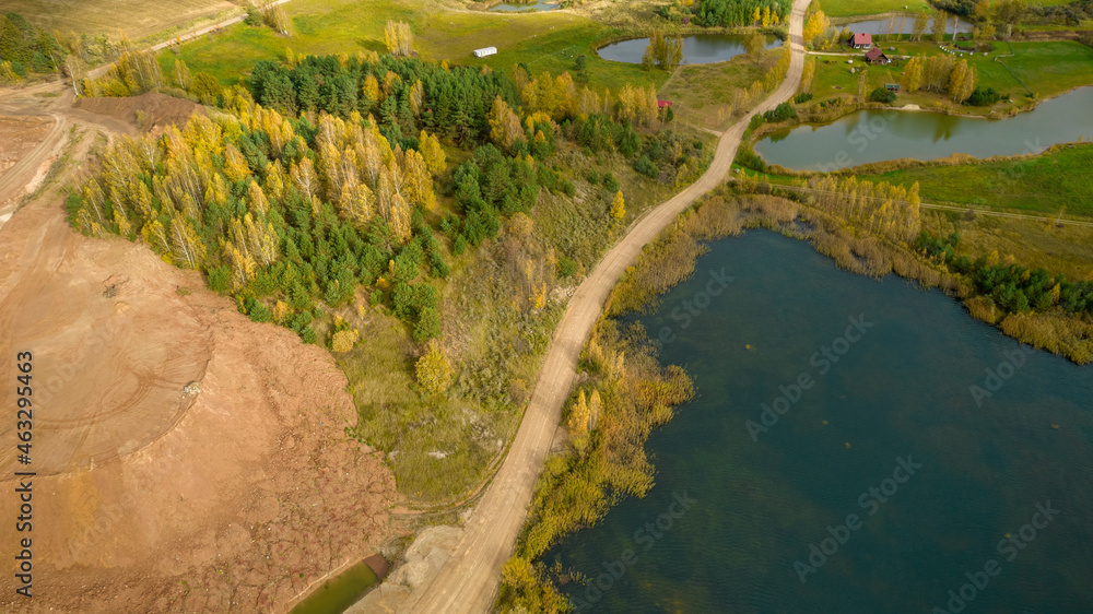 Little lake or pond of unusual shape with a beautiful autumn nature, small house and gravel road photographed from above with a drone. Real is beautiful Little lake or pond of unusual shape with a beautiful autumn nature, small house and gravel road photographed from above with a drone. Real is beautiful