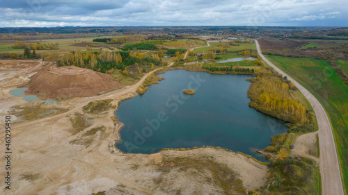 Open pit gravel mining. Little lake or pond of unusual shape with a beautiful autumn nature and gravel piles photographed from above with a drone. Real is beautiful 