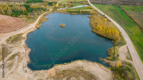 Open pit gravel mining. Little lake or pond of unusual shape with a beautiful autumn nature and gravel piles photographed from above with a drone. Real is beautiful 