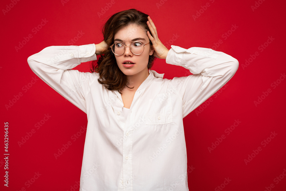 Beautiful young amazed curly brunette woman wearing white shirt and optical glasses isolated on red background with copy space. Shock concept Beautiful young amazed curly brunette woman wearing white shirt and optical glasses isolated on red background with copy space. Shock concept