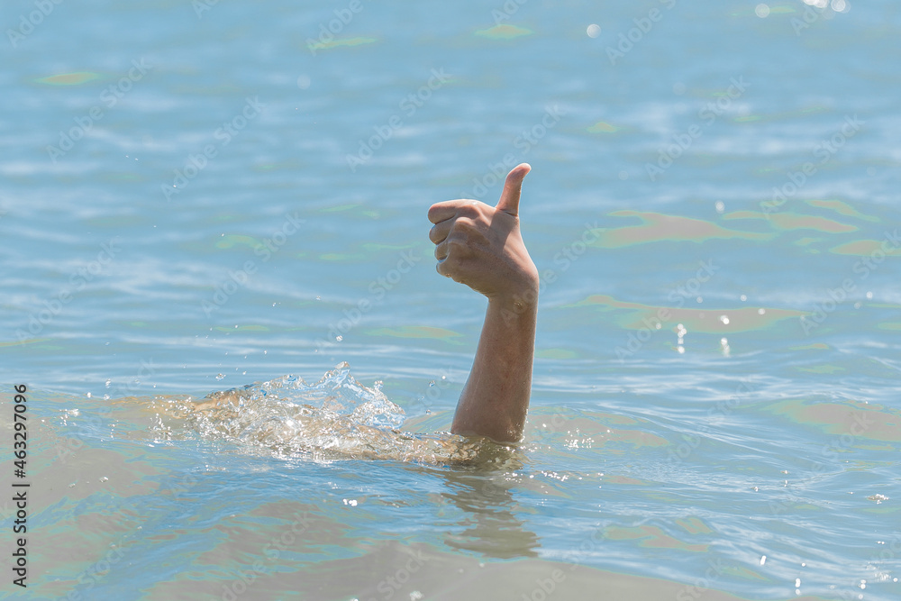 Hand from under the water of a drowning girl shows class with a thumb up. Help and urgent rescue of a person during a dangerous swimming, sos