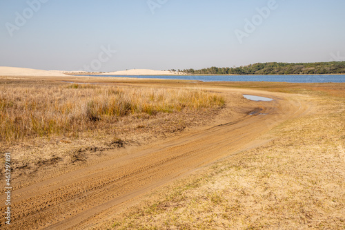 Dirty road with lake, sand and vegetation photo