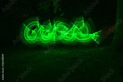 Freehand light painting in the form of green glowing curves in a dark park at night, abstract art, long exposure with motion blur, copy space, selected focus