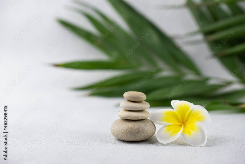 Obraz premium Pyramids of gray and white zen pebble meditation stones on white background with plumeria tropical flower. Concept of harmony, balance and meditation, spa, massage, relax