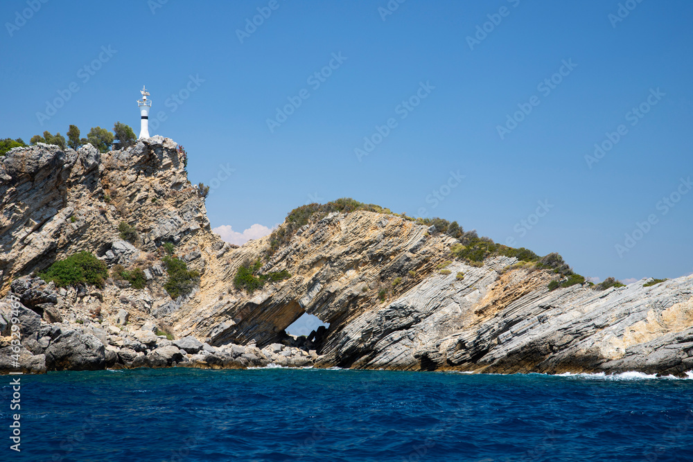 Rocky island with lighthouse and grotto in blue sea 