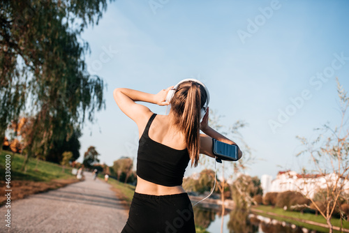 Fototapeta Naklejka Na Ścianę i Meble -  A girl in headphones is engaged in outdoor fitness in a metropolis. running and sports in summer