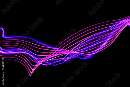 Long exposure photograph of neon colour in an abstract swirl, parallel lines pattern against a black background. Light painting photography. © LizFoster
