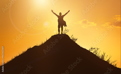 Business and success  leadership and achievement people concept. Silhouette of man on mountain top over sunset sky background. Hands up photo