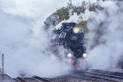 Retro steam train departs from the station wooden platform.