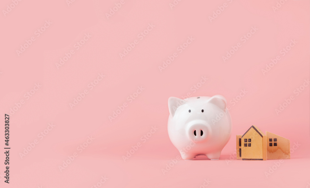 Money saving and investment concept. Piggy bank and wooden house on pink background with copy space Money saving and investment concept. Piggy bank and wooden house on pink background with copy space