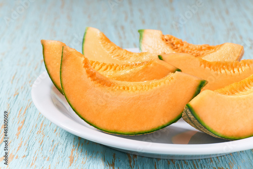 Sliced ripe melon in a ceramic plate on a wooden table.