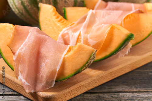 Cantaloupe melon and prosciutto ham on a wooden table.