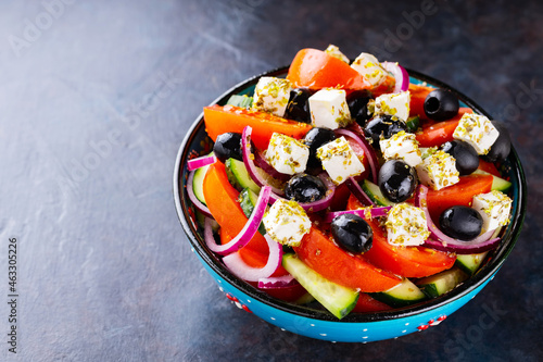 Greek salad in a bowl on a dark background. Healthy salad with feta cheese and olives. Fresh vegetable salad of Mediterranean cuisine. Copy space. Top view