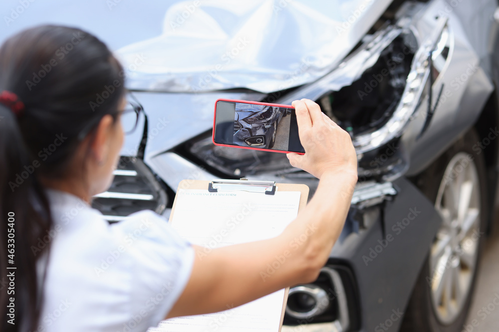 Insurance agent takes pictures of damage to car after accident on smartphone - obrazy, fototapety, plakaty 
