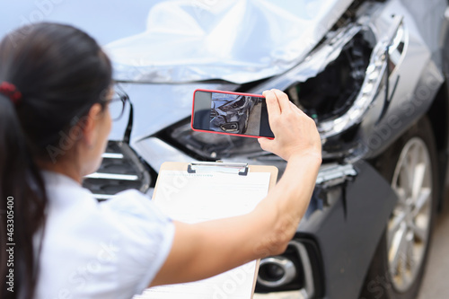 Insurance agent takes pictures of damage to car after accident on smartphone