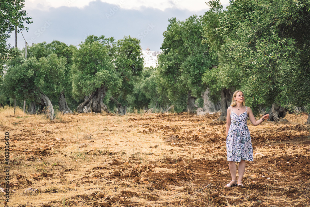 Blonde hair girl walking in a beautiful secular olive trees agricultural field similar to a sculpture in autumn
