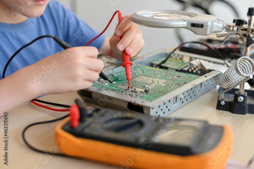 Young wunderkind diagnosing and fixing broken circuit board with multimeter