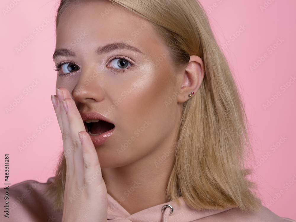 cute young blonde in a pink hoodie is shocked and surprised, says wow. The emotion of surprise, hands touching the face. portrait on a pink background, close-up cute young blonde in a pink hoodie is shocked and surprised, says wow. The emotion of surprise, hands touching the face. portrait on a pink background, close-up