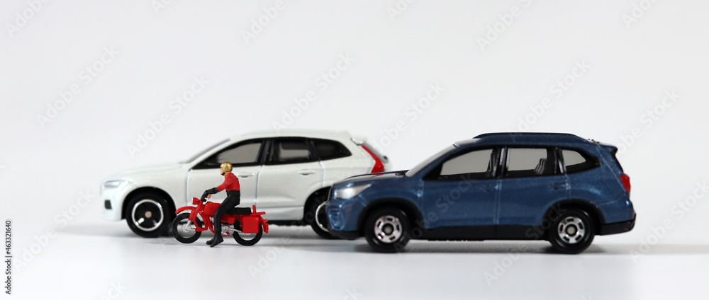 A motorcycle driver between a blue car and a white car. Miniature people and miniature cars.
