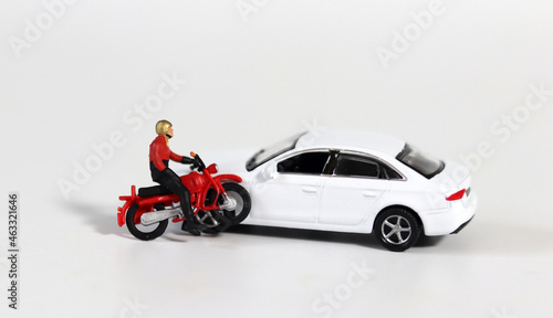 Miniature people and miniature car. A miniature motorcycle rider in front of a white miniature car. Concept about a dangerous motorcycle accident