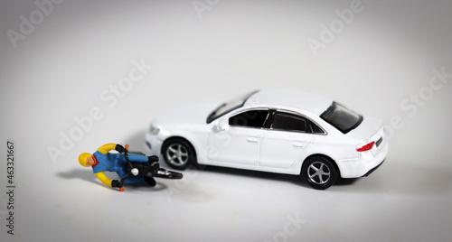 Miniature people and miniature car. A miniature motorcycle driver who fell in front of a white miniature car. Concept about a dangerous motorcycle accident. 