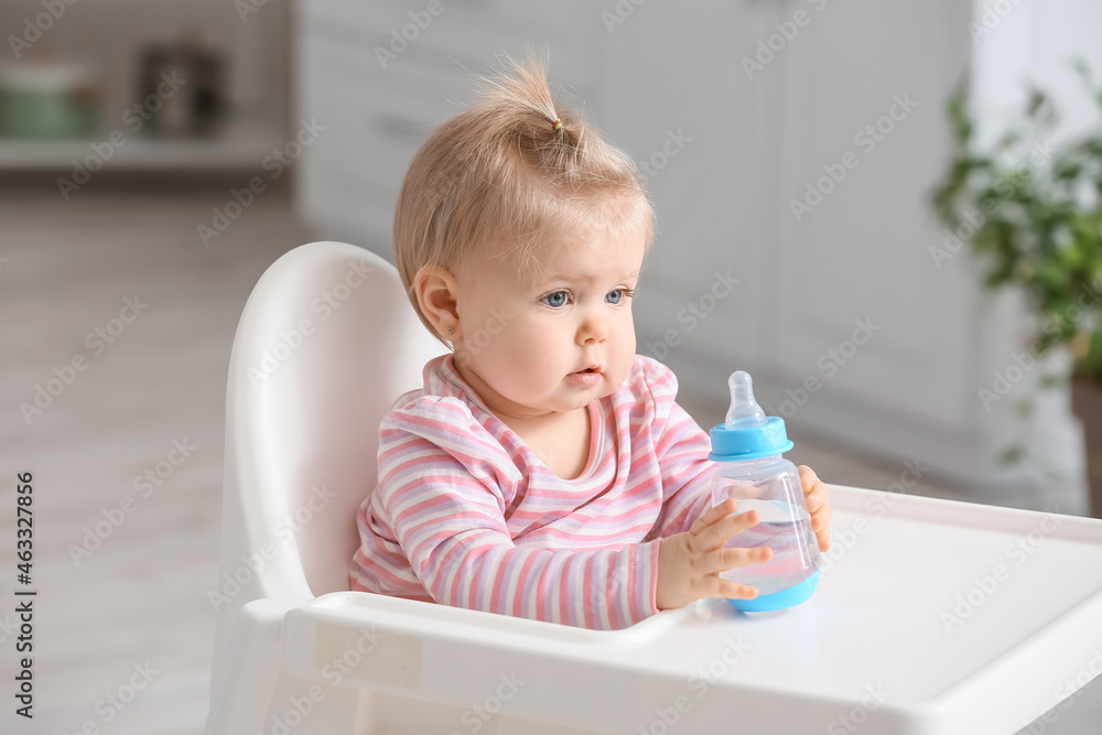 Cute baby girl with bottle of water sitting on high chair in kitchen Cute baby girl with bottle of water sitting on high chair in kitchen