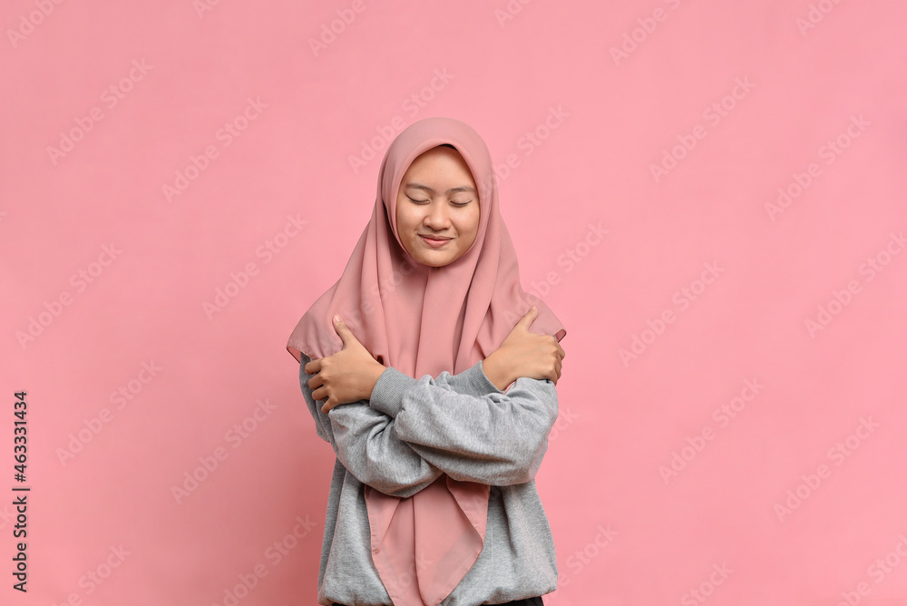 Young pretty muslim woman feeling in love, smiling, cuddling and hugging self, staying single Young pretty muslim woman feeling in love, smiling, cuddling and hugging self, staying single