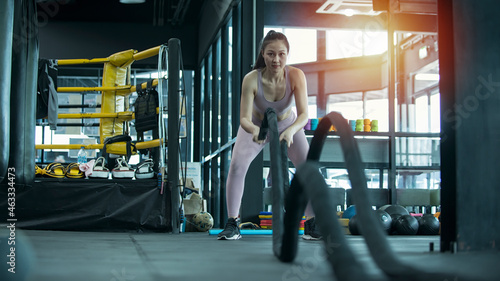 Woman doing cross fit exercise with one battle rope in gym. person exercising in gym. Woman training with battle rope in cross fit gym.